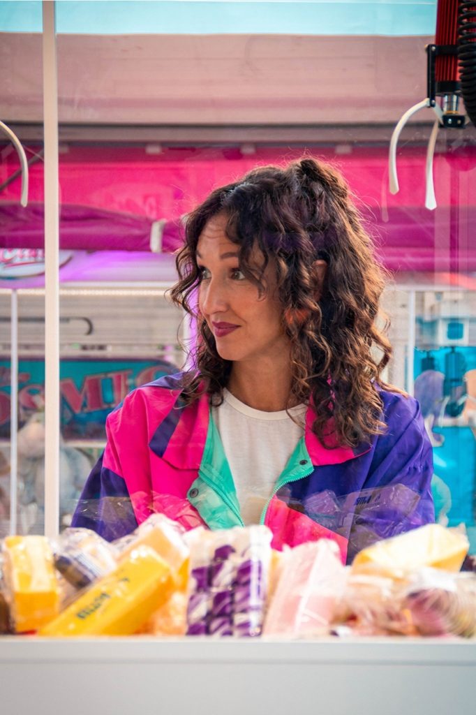 Cora Tellaa de profil devant un stand de confiseries, à la fête foraine